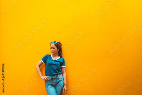portrait of fashion hipster girl wear sunglasses standing beside wall yellow with posing relaxing smile by wearing blue shirt and blue jeans