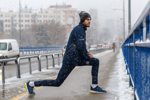 Young man stretching before running in city street at cold winter day.