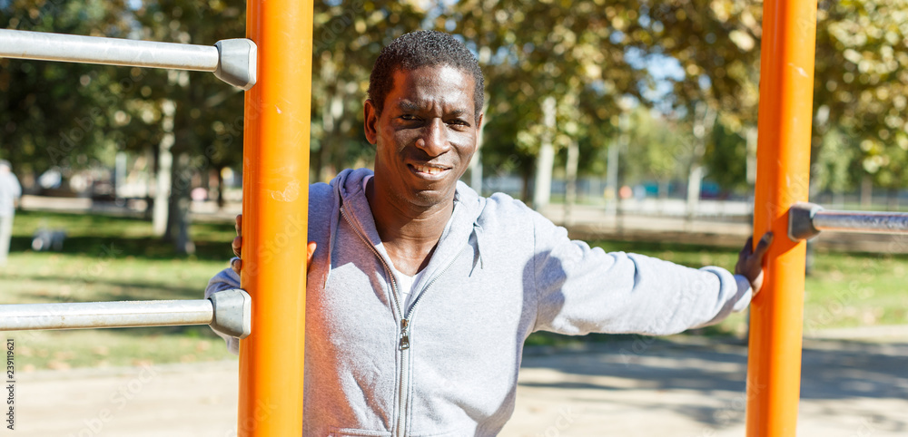 Fototapeta premium Young male training different exercises at chin-up bar in park outdoor