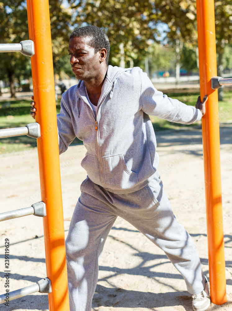 Fototapeta premium Young male training different exercises at chin-up bar in park outdoor