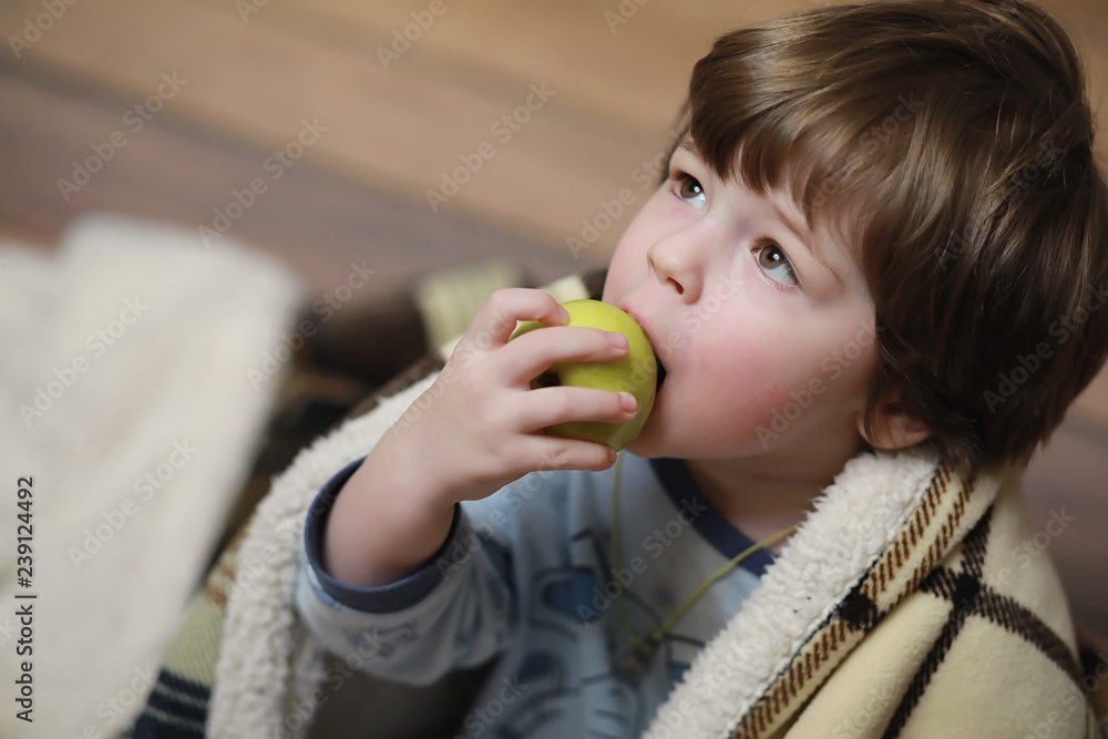 Portrait of a small curly-haired boy. A child wrapped in a rug eats an apple. A two-year-old boy hides under a blanket. Portrait of a small curly-haired boy. A child wrapped in a rug eats an apple. A two-year-old boy hides under a blanket.