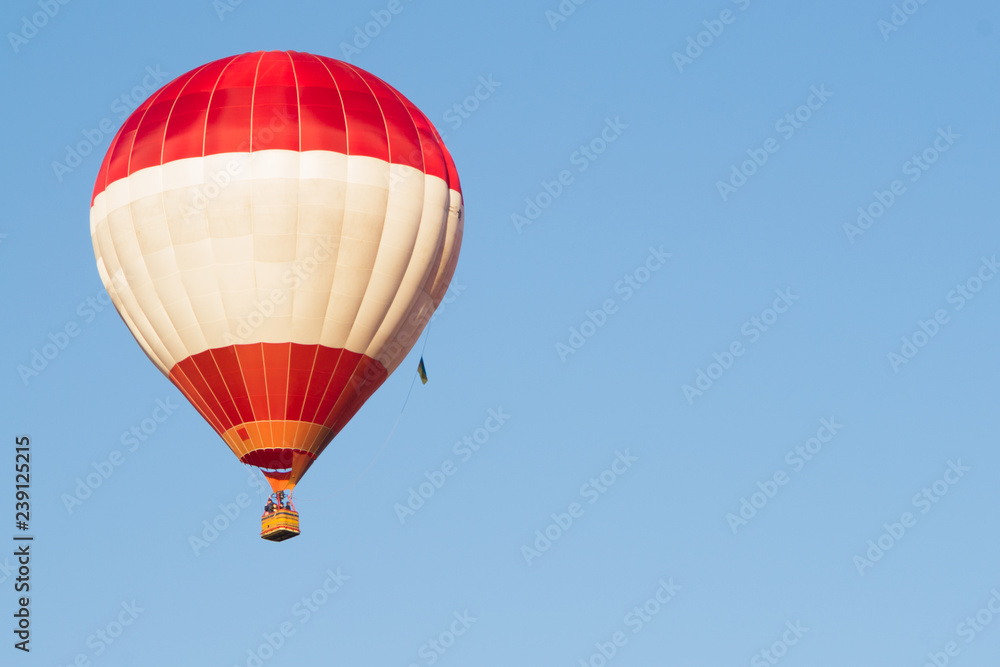 Naklejka premium Red balloon against a blue sky. Aerostat. People in the basket. Fun. Summer entertainment. Romantic adventures.