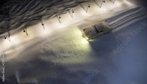 Lonely Car driving on a snow covered road with street lamps in snowy weather at night. Artwork decoration for greeting card. New Year concept