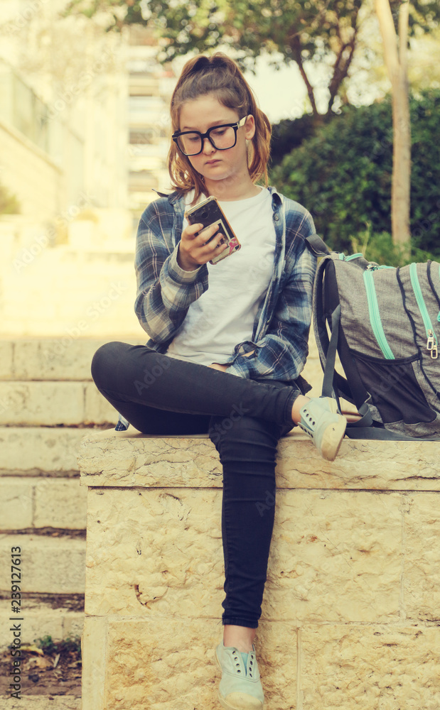 Obraz premium Portrait of tenage girl sitting outdoor with mobile phone