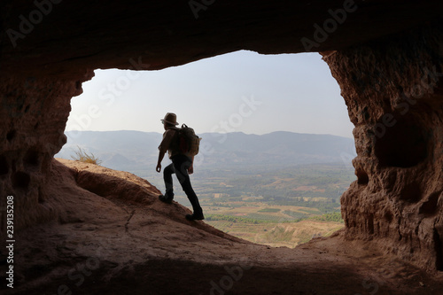 MOUNTAINEER WITH HAT AND BACKPACK LEAVING A CAVE IN THE HIGH OF THE VALLEY ON SUMMER HOLIDAY