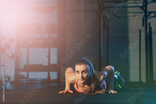 Fit woman in colourful sportswear doing burpees on a exercise mat in a grungy industrial type space