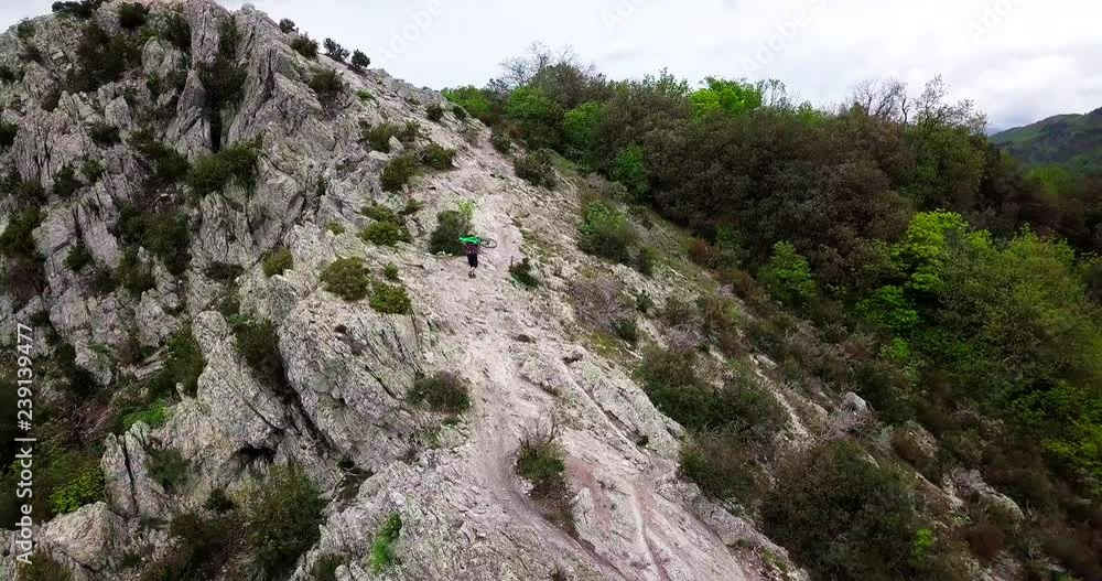 Aerial shot of a mountain biker lifting his bike on top of the mountain.