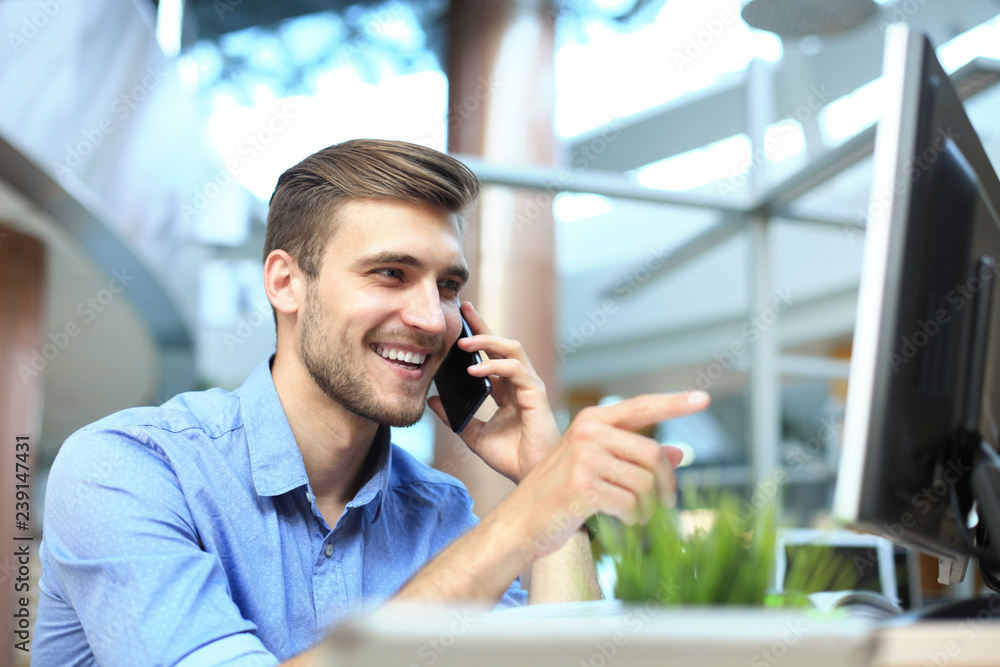 Smiling businessman sitting and using mobile phone in office. Smiling businessman sitting and using mobile phone in office.