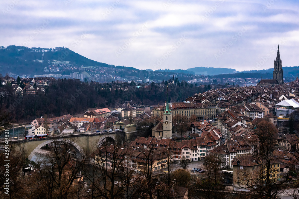 Historical Old Town of Bern city, tiled roofs, bridges over Aare river and church tower on cloudy day, Switzerland