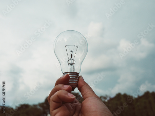 Concept save energy efficiency. Hand holding light bulb on blurred tree and sky background