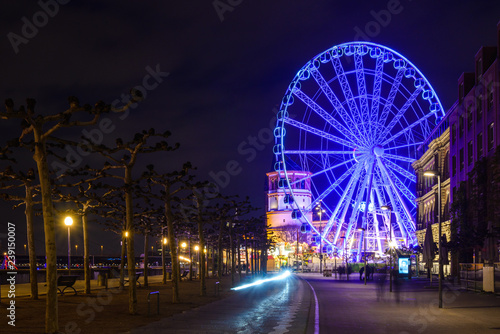 Night scenery on promenade and walkway along riverside of Rhine river and background of Ferris wheel of Christmas market festival, Weihnachtsmarkt, in Düsseldorf, Germany.