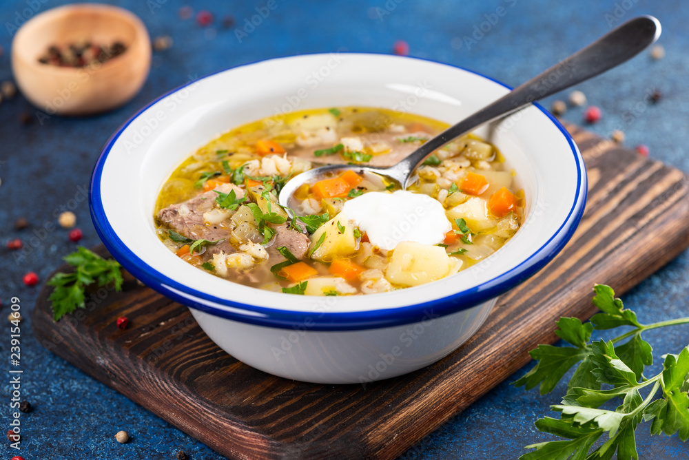 Rassolnik - Traditional Russian soup with pickled cucmbers, pearl barley, meat, pickles, carrots and potatoes on blue background. Top view
