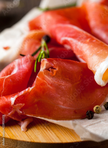 Closeup of thin slices of prosciutto with mixed olives and paprika on wooden cutting board