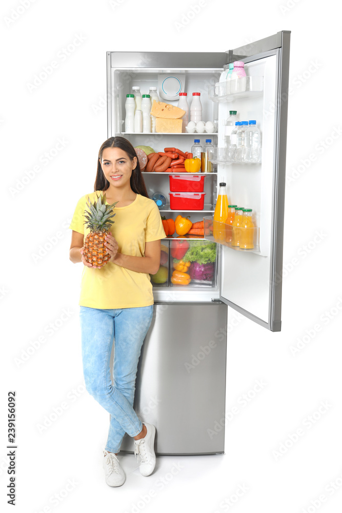 Young woman with pineapple near open refrigerator on white background Young woman with pineapple near open refrigerator on white background