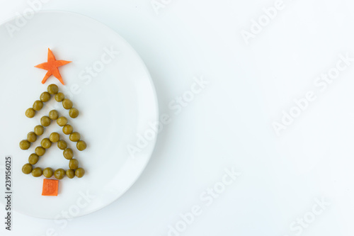 Fir tree made of peas and carrots on white plate on rustic white table background. New year and christmas concept, creative idea of celebratory meal