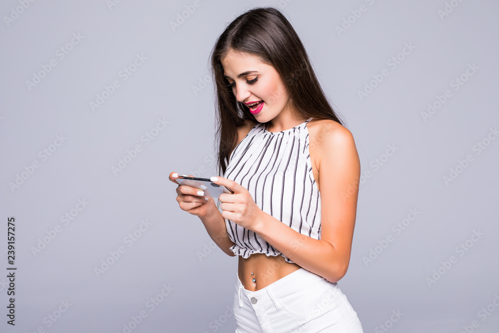 Happy attractive brunette girl joying win in video game on smartphone isolated over gray background Happy attractive brunette girl joying win in video game on smartphone isolated over gray background