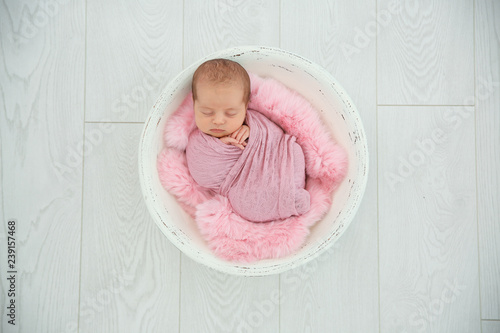 Adorable newborn girl lying in baby nest on light background, top view