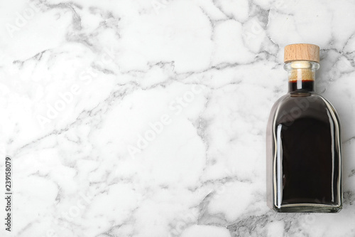 Balsamic vinegar in glass bottle on marble background, top view. Space for text