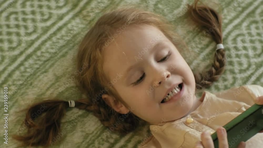 happy girl child with blond hair and pigtails, lying on the sofa, using the phone, smiling, portrait happy girl child with blond hair and pigtails, lying on the sofa, using the phone, smiling, portrait