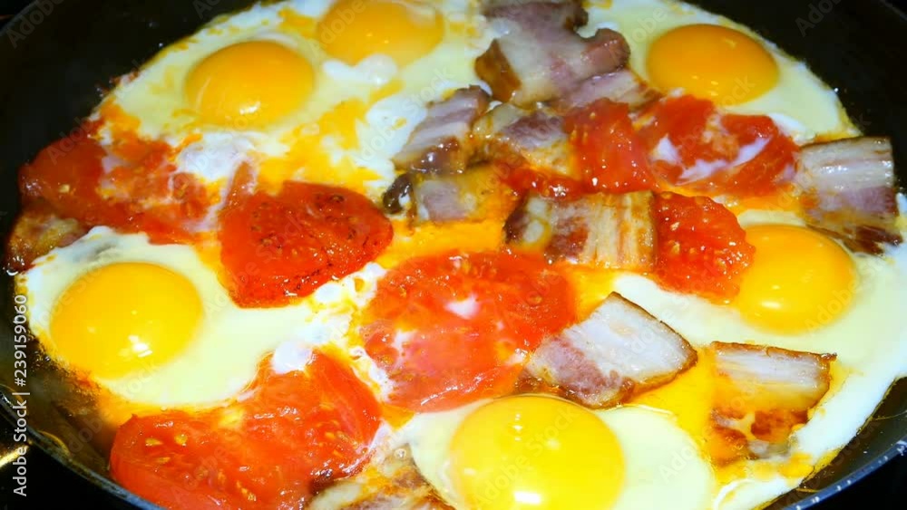 Traditional breakfast. Eggs with tomatoes and bacon are fried in a frying pan. Yellow egg yolks. Traditional breakfast. Eggs with tomatoes and bacon are fried in a frying pan. Yellow egg yolks.