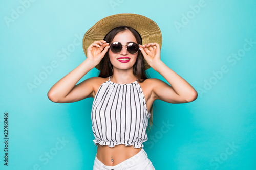 Elegant young attractive woman wearing straw hat and sunglasses, thinking about her summer vacation isolated over pastel blue background.