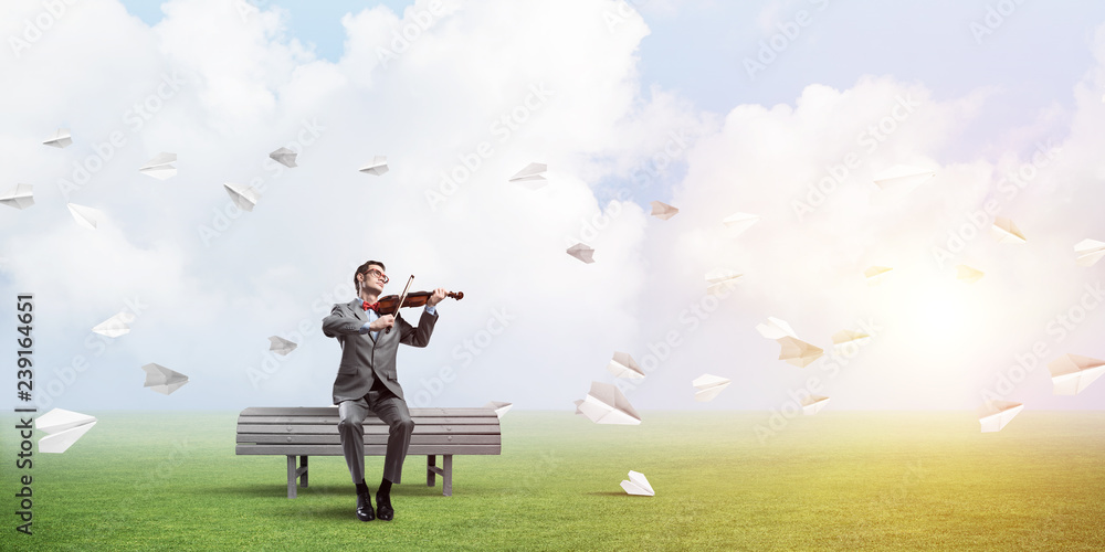 Handsome violinist in park on wooden bench play his melody