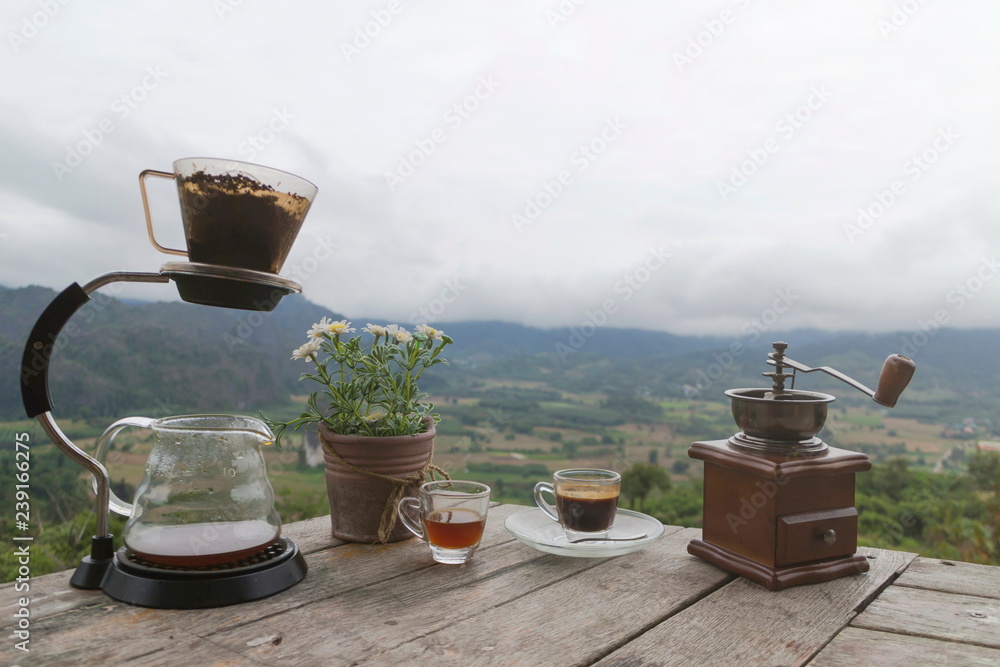 Morning cup of coffee with Rotary Coffee Grinder and Flower Pot on the wooden table with mountain background at sunrise and sea of mist, image with copy space.