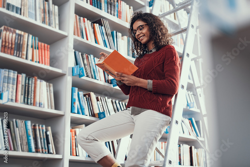 Positive smiling lady sitting on the step ladder and reading