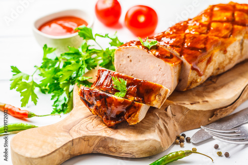 Baked meatloaf with greens and barbecue sauce on a wooden board, white background.