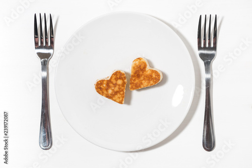 plate of pancakes in the shape of heart and two forks on white background, top view