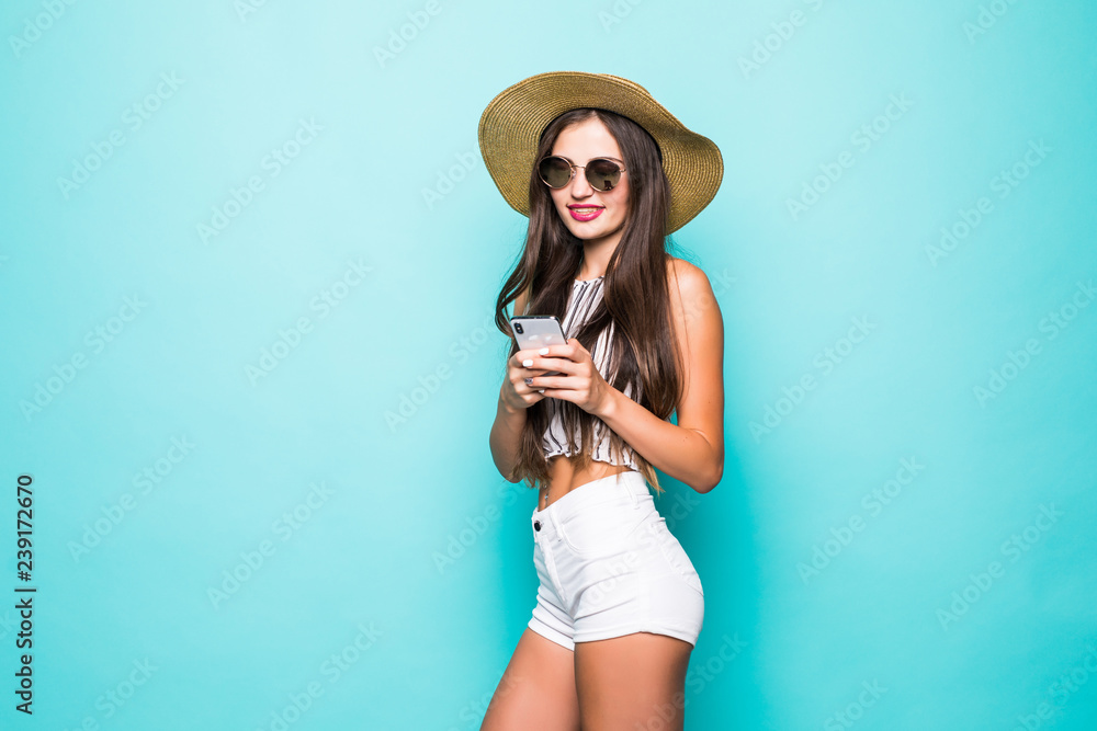 Portrait of a smiling young woman in summer hat using mobile phone isolated over blue background Portrait of a smiling young woman in summer hat using mobile phone isolated over blue background