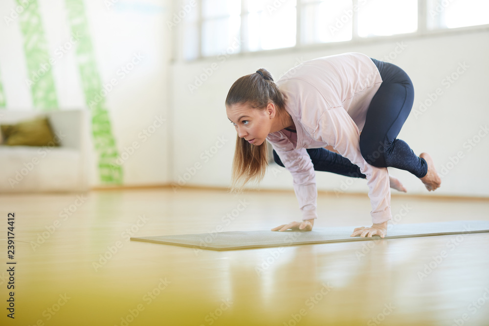Fototapeta premium Young performer in activewear standing on her hands while hanging over floor during yoga training in gym