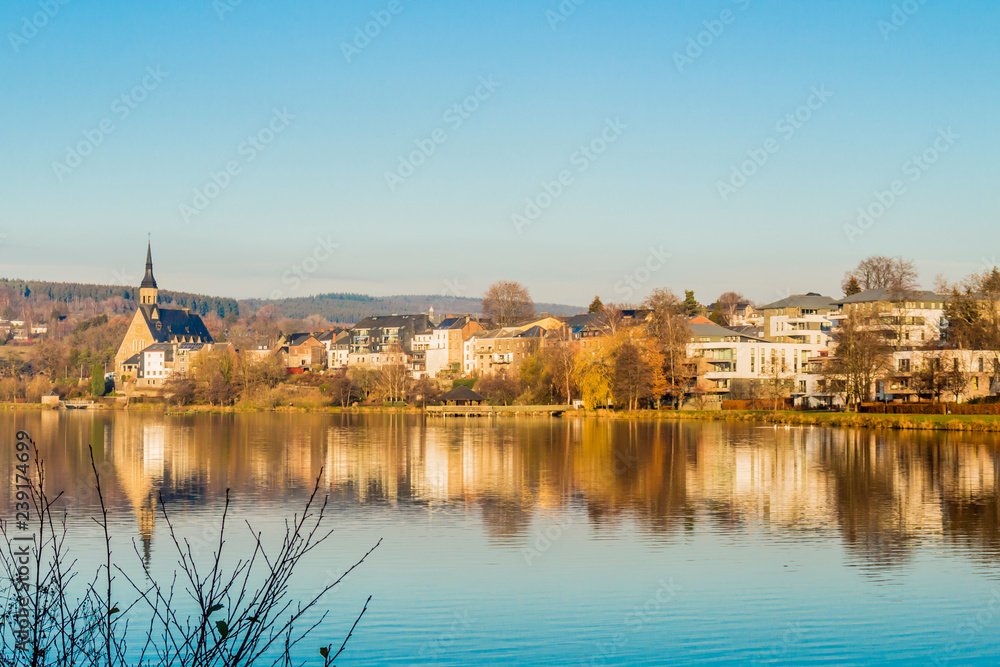 beautiful view of the village of Vielsalm and its St Gengoul church with a blue sky and the Doyards lake with a amazing reflection in the water on a wonderful cold winter day in the Belgian Ardennes