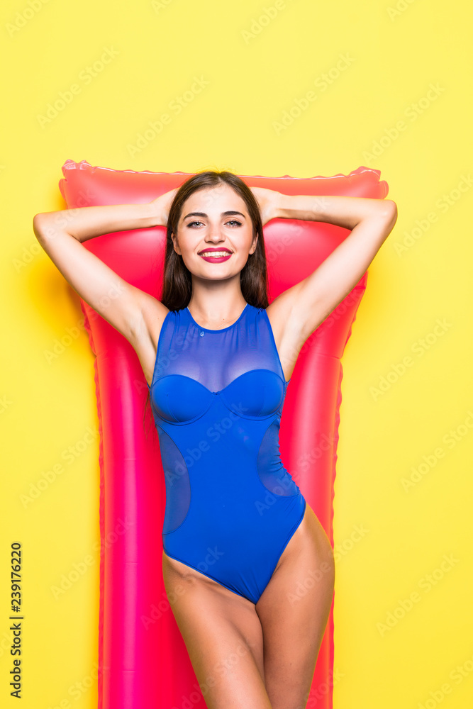 Young beautiful smiling woman in sunglasses and bikini with pink inflatable mattress on yellow background Young beautiful smiling woman in sunglasses and bikini with pink inflatable mattress on yellow background
