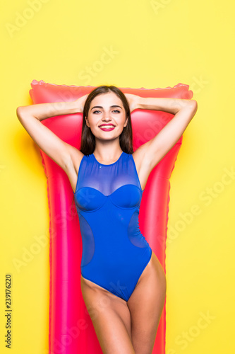 Young beautiful smiling woman in sunglasses and bikini with pink inflatable mattress on yellow background © dianagrytsku