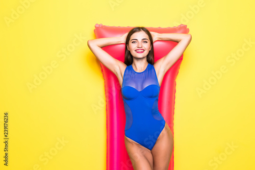 Young attractive woman in bikini posing with pink inflatable mattress, isolated on yellow background © dianagrytsku