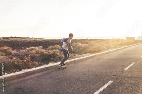 Active young teenager boy doing skateboard activity with skate board on a long asphalt road with sunset light in background - sport training for trendy people - california youth concept