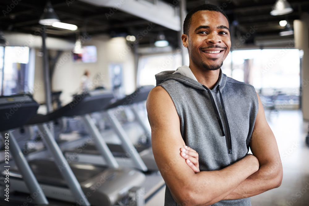 Φωτογραφία Happy young sportsman with his arms crossed on chest standing by sports equipmen