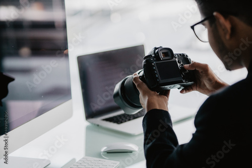 Young cheerful photographer man use photocamera while working in his office photo