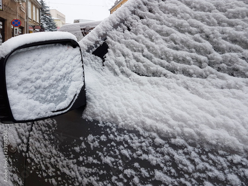 Snow-covered cars in the winter. Frozen mirror of a passenger car. Cold weather. Dirty road traffic.