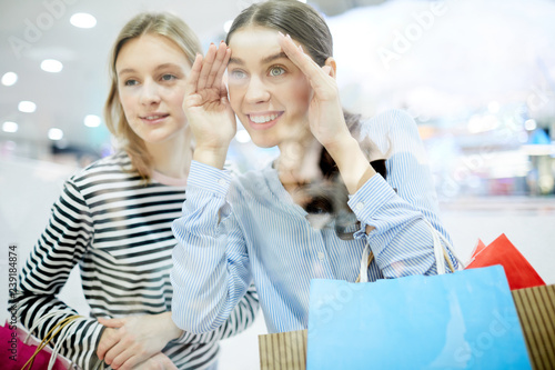 Pretty shopper peering in shop window while hanging around mall with her friend on weekend © pressmaster