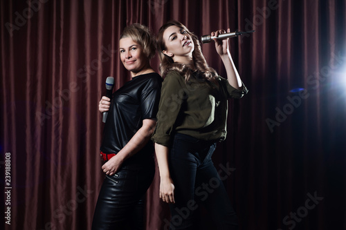 Women singing on stage in the karaoke microphones on the background of the red curtains