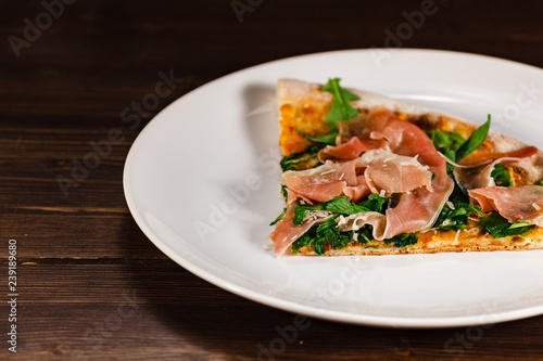 Piece of pizza with ham and vegetables on wooden table