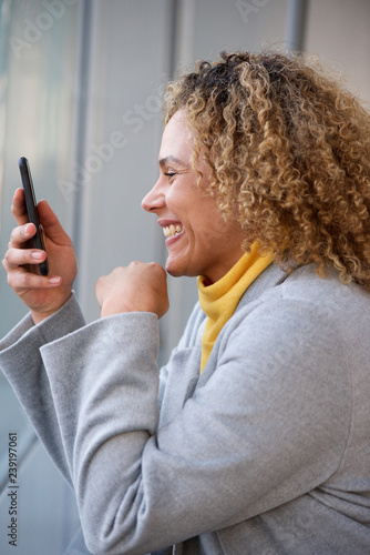 happy african american woman with curly hair looking at mobile phone