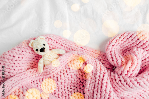 A small knitted baby toy-bear is covered with a warm blanket, flat lay, top view