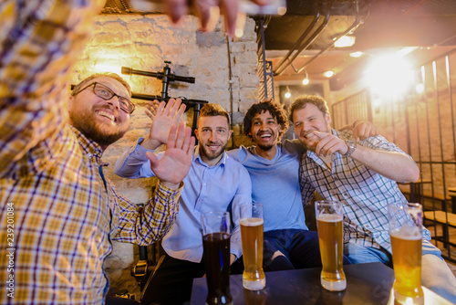 Four happy male friends having a picture of them while sitting in a bar and drinking beer.