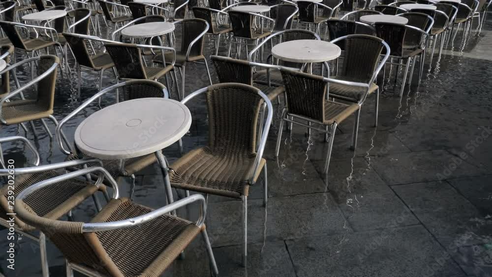 Flooded restaurant tables and chairs on San Marco piazza or square. No people. Close Up view. Day light reflected in water. Small quiet waves on water because of light wind or breeze. Venice, Italy Flooded restaurant tables and chairs on San Marco piazza or square. No people. Close Up view. Day light reflected in water. Small quiet waves on water because of light wind or breeze. Venice, Italy