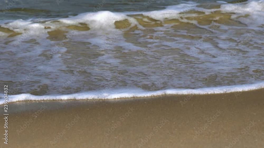 Slow motion close up view of beautiful sea wave foam washing smooth sandy beach. Quiet crystal clear sea and small turquoise waves at shore on amazing sunny summer day Slow motion close up view of beautiful sea wave foam washing smooth sandy beach. Quiet crystal clear sea and small turquoise waves at shore on amazing sunny summer day