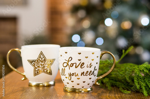 Two cups with text in Christmas interior with lights on background.