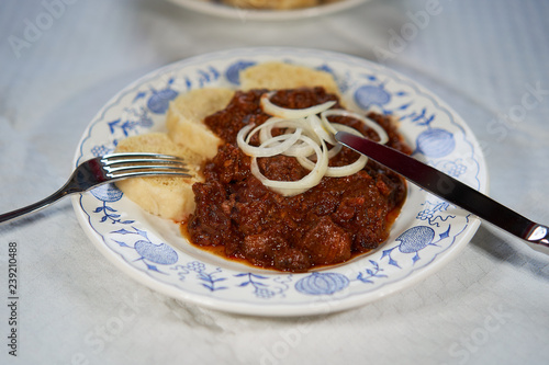 Fototapeta Naklejka Na Ścianę i Meble -  Slow cooked czech or hungarian beef goulash stew served with traditional czech dumplings and choped fresh onion on the rustic plate with stainless steel fork and knive.